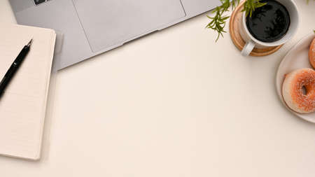 Modern minimal white office desk top view, flat lay with a copy space, coffee cup, laptop computer, doughnut, pen and spiral notepad.の写真素材