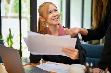 Cheerful asian young female office worker employee smiling while talking with her friendly female...
