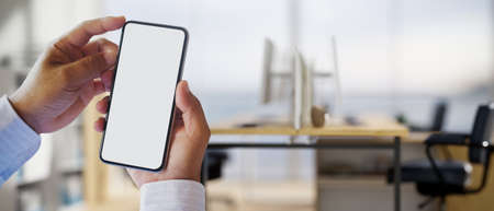 Close-up image, A businessman hands holding a smartphone cellphone white screen mockup over blurred...