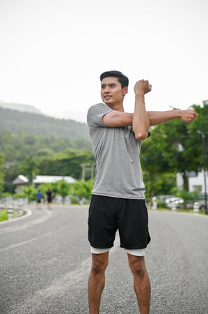 Portrait of a handsome asian young man in active and comfy sportswear stretching his arms and body before running, training or jogging.の写真素材