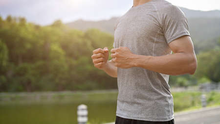 Active Asian millennial man in a sportswear running or jogging in the beautiful green park. Sport...