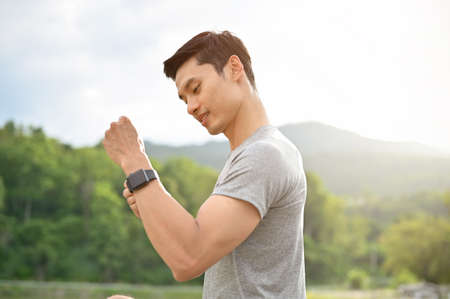 Sporty and handsome Asian man in a sportswear with his sport smartwatch, jogging or running in the...
