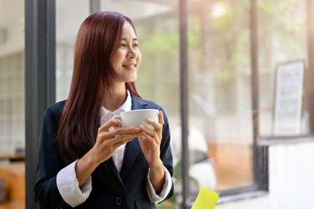 Portrait of a relaxed and pleased asian businesswoman holding a coffee cup, sipping morning coffee...