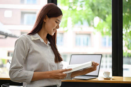 Attractive young asian businesswoman reading a book while sitting in the coffee shop. Young female college student reading book, researching some information on the textbook.の写真素材