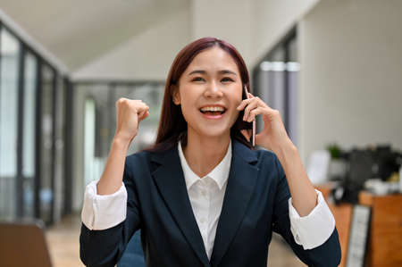 Young Asian businesswoman received good unexpected news on the phone call in the office. Work promotion, Job offer, Great newsの写真素材