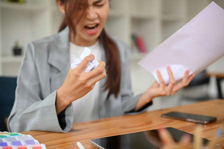 Mad angry asian businesswoman or female boss crumpling a document paper, yelling in the office,...