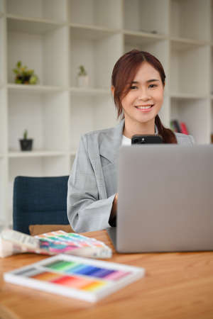 Portrait of a happy asian female graphic designer or interior designer sits at her office desk,...