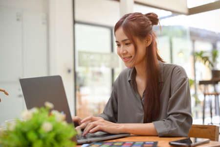 Creative young asian female graphic designer sits at office desk, working on her task and using portable laptop computer.の写真素材