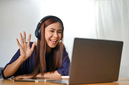 Cheerful and attractive Asian female tutor is tutoring her students on online meeting via laptop...