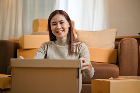 Happy millennial Asian woman packing her stuff in a cardboard box in the living room. House moving conceptの写真素材