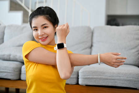 Portrait of an attractive young Asian woman in sportswear stretching her arms, exercising in the...