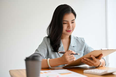 Successful asian businesswoman or female executive manager reading a business document, reviewing the business report in the office.の写真素材