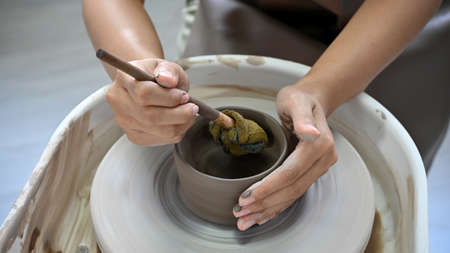 A female hands using a scrapper, making a ceramic cup on potter's wheel. Artisan production. cropped...