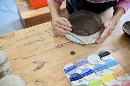 Top view, Professional asian aged woman making a ceramic plate, decorating her plate on the...