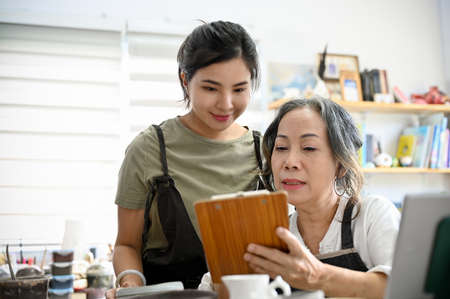 Professional asian aged woman coaching and showing the moulding clay instruction on the paper to young female student in the workshop.の写真素材