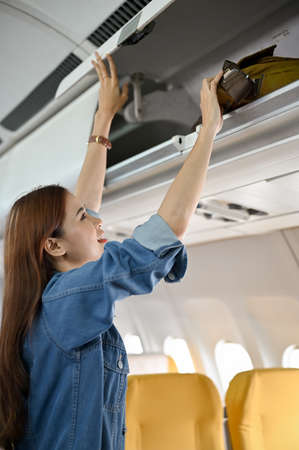 Beautiful young asian woman putting her bag at overhead locker or overhead compartment. Female...