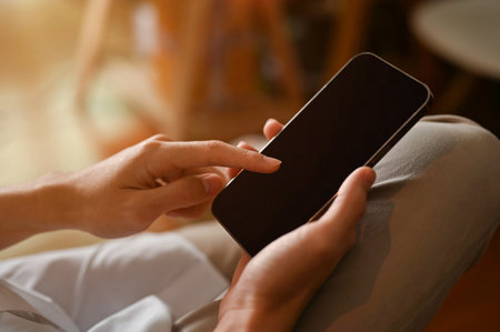 Close-up image and focus hands. Male sitting on the chair and using modern smartphone in the coffee shop. Phone black screen mockup.の写真素材