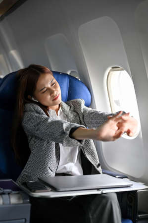 Beautiful asian young businesswoman stretching arms, feeling uncomfortable and tired during a long flight flying to another country. Business trip conceptの写真素材