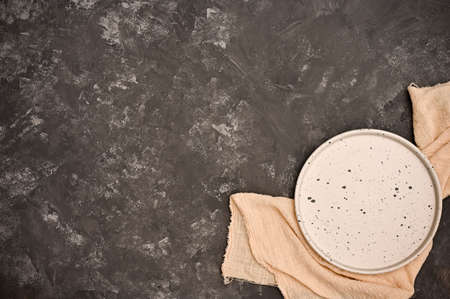 Restaurant table, dining table setting concept. Empty white craft ceramic plate on beige napkin and copy space on dark grey cement tabletop.の写真素材