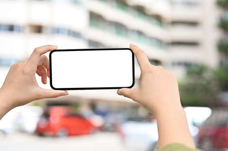 Close-up image, A female hands holding a smartphone white screen mockup over blurred apartment building in the background.の写真素材