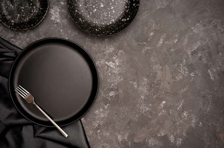 Craft ceramic handmade concept. Empty black ceramic plate on black dining table background. top view