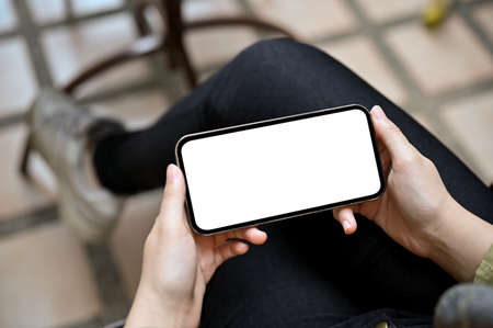 A female hands holding a smartphone in horizontal way, watching some video clip on the internet, playing mobile game. Phone blank screen mockup.の写真素材