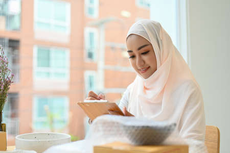 Beautiful young asian muslim female entrepreneur noting an order on her notepad, preparing shipment product in the office.の写真素材