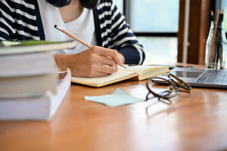 Cropped image, Female college student doing homework, writing something on notebook, researching...