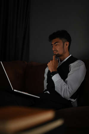 Serious and thoughtful Asian businessman or male executive manager looking at laptop screen,...