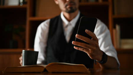 A successful smart asian businessman in the office sipping morning coffee and using his smartphone....