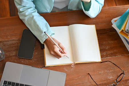 Overhead shot of a young female high school student or college student doing homework, writing diary and taking notes on blank notebook.の写真素材