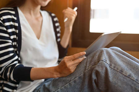 Female college student in casual outfit sitting in a campus library, using a portable tablet touchpad. cropped, closeup imageの写真素材