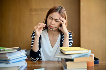 Pretty young Asian female college student having a migraine, headache and eyes strain from reading...