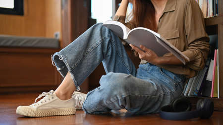 A young female college student sitting in the library floor and reading a book. cropped image....