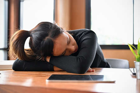 Tired sleepy young Asian female worker or college student sleeping on the desk. Exhausted from overworked.の写真素材