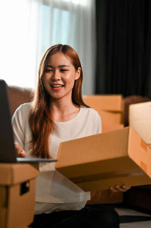 Portrait of a beautiful millennial asian female SME business owner updating her stock and shipping...