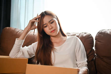 A thoughtful Asian young female online shop owner is packing a customer's packages in the living...