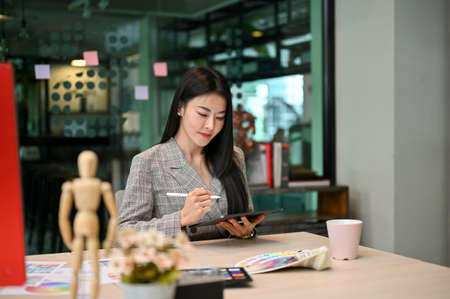 Successful and confident Asian female graphic designer manager using digital tablet to design her...