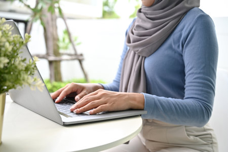 cropped image, Young Asian Muslim woman wearing hijab, sitting in her house backyard and using...