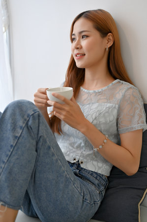 Portrait, Beautiful and charming millennial Asian woman relaxes sipping morning hot coffee or tea in her living room.の写真素材