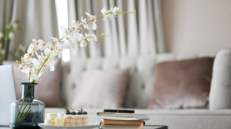 Modern luxury home living room with comfortable sofa, flowers in a ceramic vase, book, a plate of dessert and decor on coffee table. close-up imageの写真素材