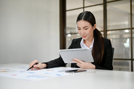 Attractive and charming young Asian businesswoman or financial worker in formal suit using tablet and working with her financial report in the office.の写真素材