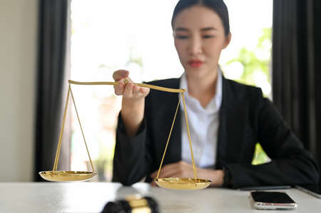 Professional asian female lawyer or attorney holding a scales of justice at her office desk. Selective focus the scales of justice.の写真素材