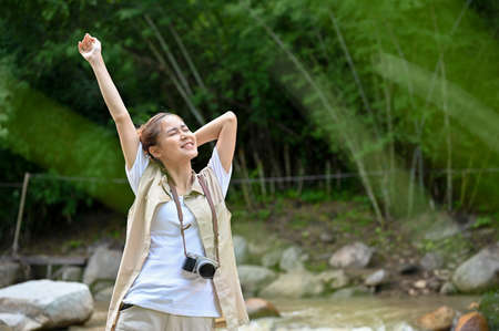 Happy and relaxed young Asian female traveler in the forest getting some fresh air to refresh her...