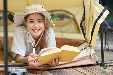 Beautiful and attractive young asian female laying in her camping tent and reading a novel. Outdoor activity concept.の写真素材