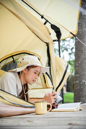 Attractive young Asian woman relaxes laying in the camping tent and reading a book at the natural...