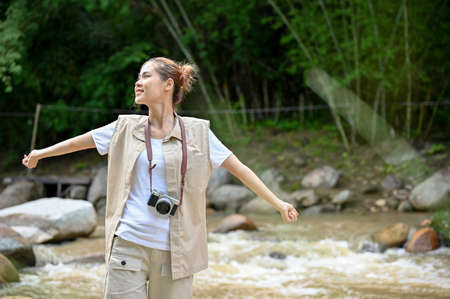 Beautiful young Asian female traveler standing near the river and getting some fresh air to refresh...