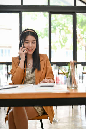 Portrait of a charming young Asian businesswoman or female marketing employee on the phone with her client in the office.の写真素材