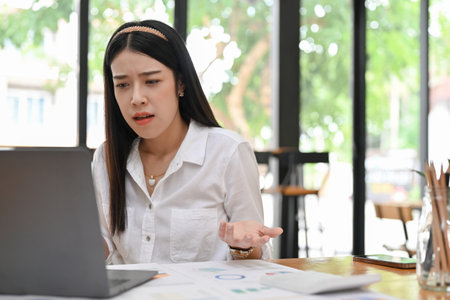 Stressed millennial Asian businesswoman or female office worker having a problems on her work assignment while using laptop computer in the office.の写真素材