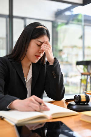 Stressed young Asian female lawyer sits at her desk in the office, having a serious trouble with her...